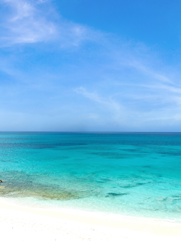 Bright blue sky, clear turquoise waters, and a small boat anchored off the shore of a Bahamas beach. 